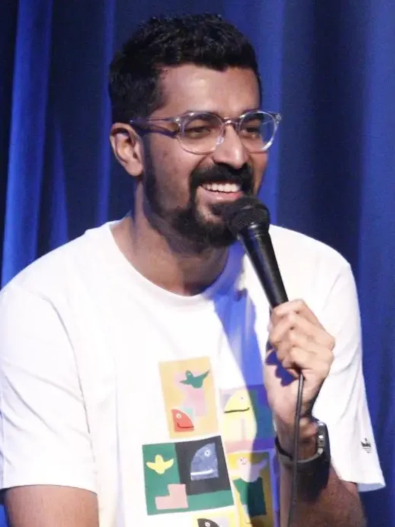 Azeem Banatwalla performing stand-up comedy in front of blue curtain