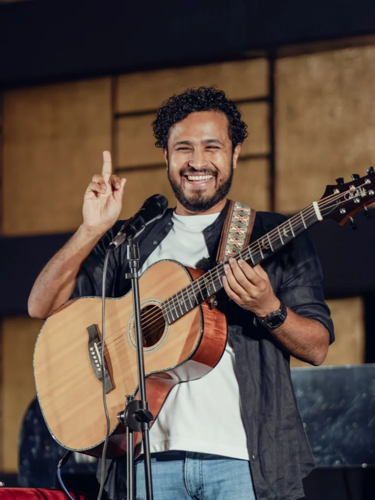 Abish Mathew performing with an acoustic guitar during a live comedy show.